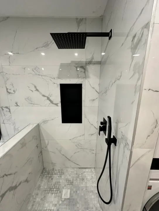 Walk-in shower beside a built-in tub with black rain head, hand shower, and white marble-look tile