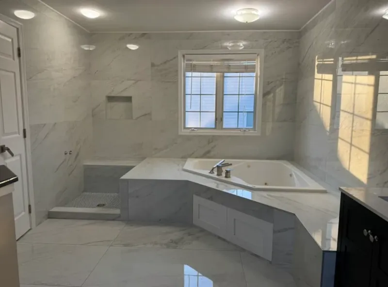 Bright finished bathroom with a large tiled tub deck, white marble-look walls, and a black vanity