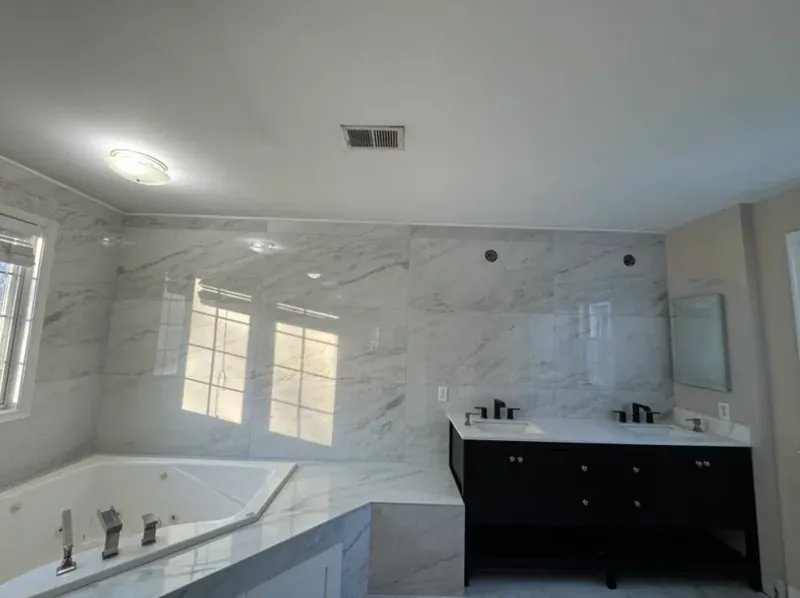 Bathroom showing white marble-look walls, a black vanity, tub deck, and window light