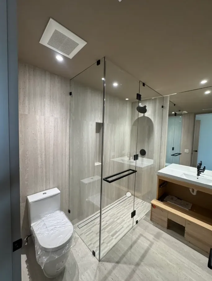 Finished bathroom with a clear glass shower enclosure, pale vertical wall tile, gray mosaic floor, and vanity