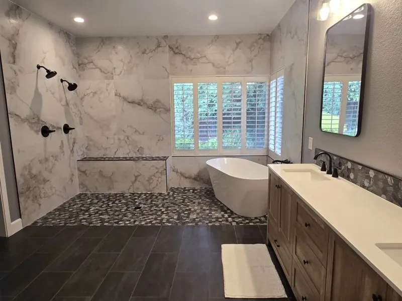 Finished bathroom with a freestanding white tub, white marble-look walls, a dark mosaic wet-zone accent, and wood vanity