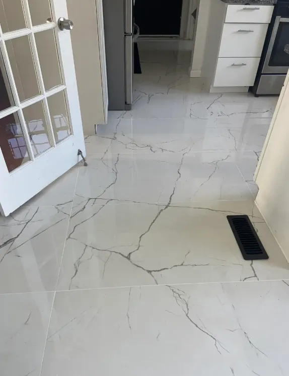 Light marble-look floor tile running from a glass-paneled doorway toward white bathroom cabinetry