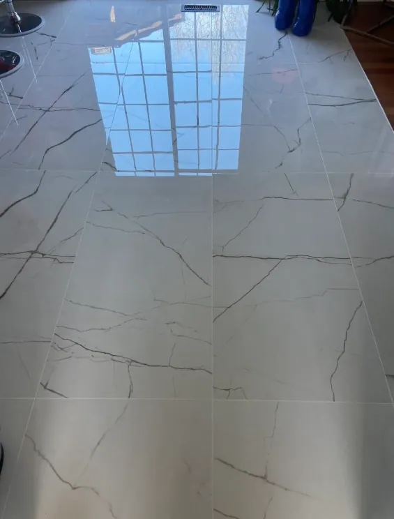 Close view of large white marble-look floor tiles with gray veining and window reflection