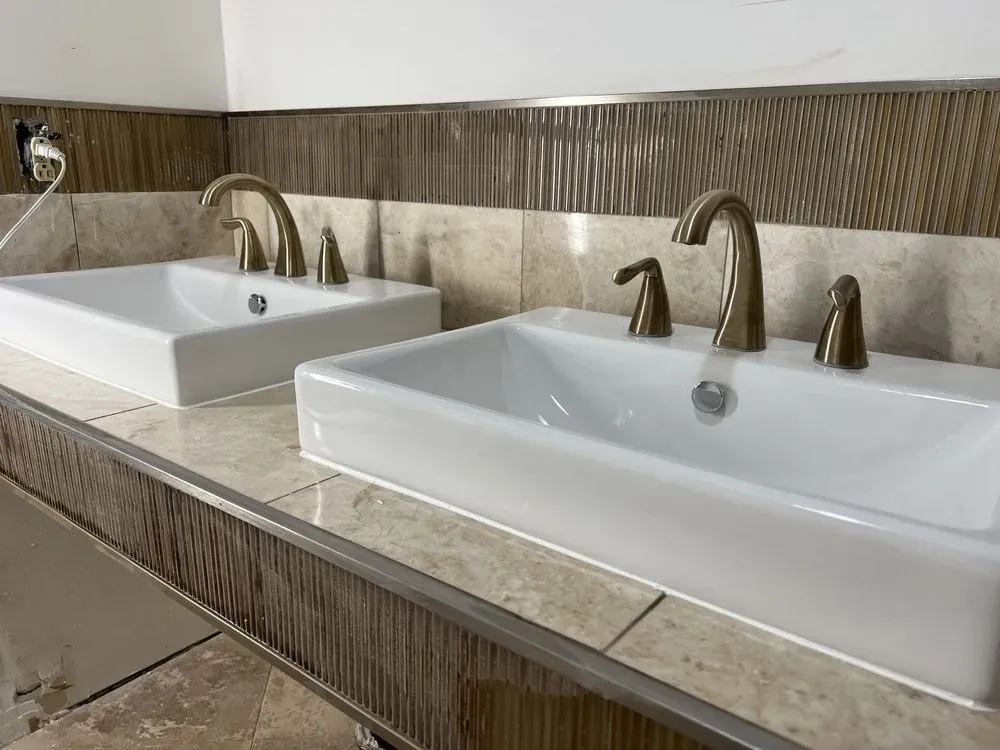 Double-vanity counter with two white vessel sinks, warm stone-look tile, and dark vertical accent band
