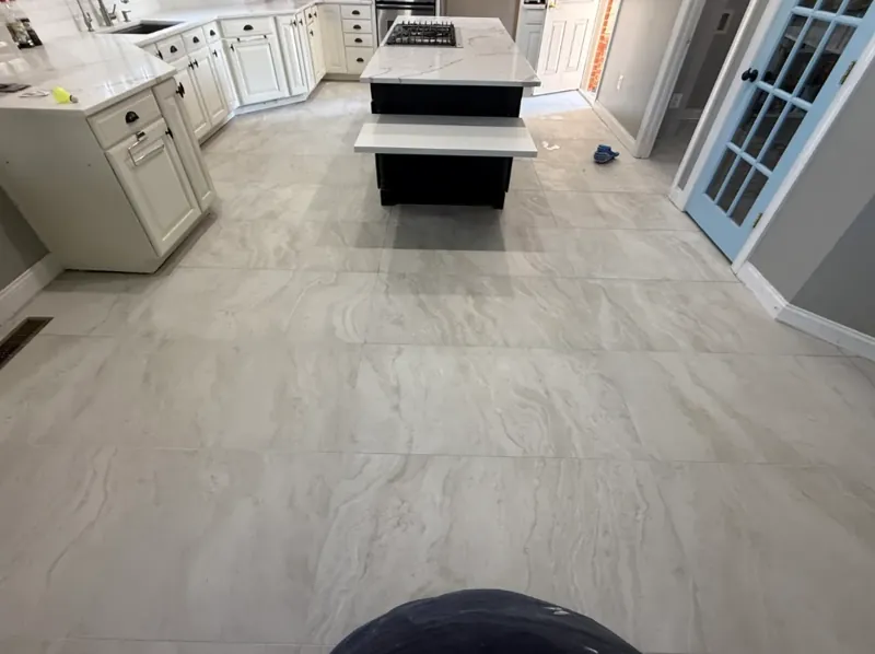 Kitchen floor view showing large light veined tiles leading toward white cabinetry and a dark island